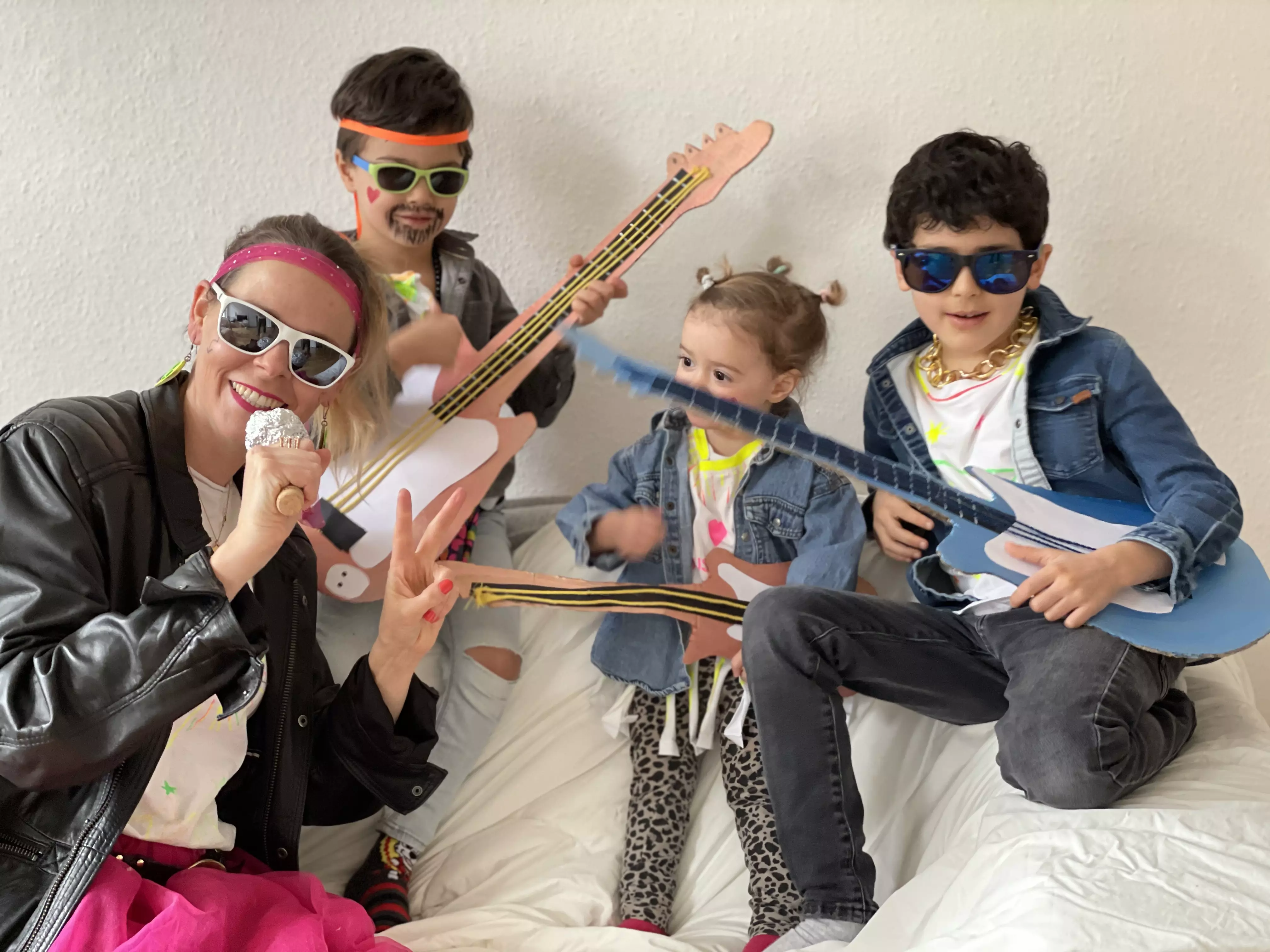 Eine Mama und drei Kinder verkleidet als Rockstars mit Sonnebrillen, Lederjacken, Jeanshemden und Papiergitarren