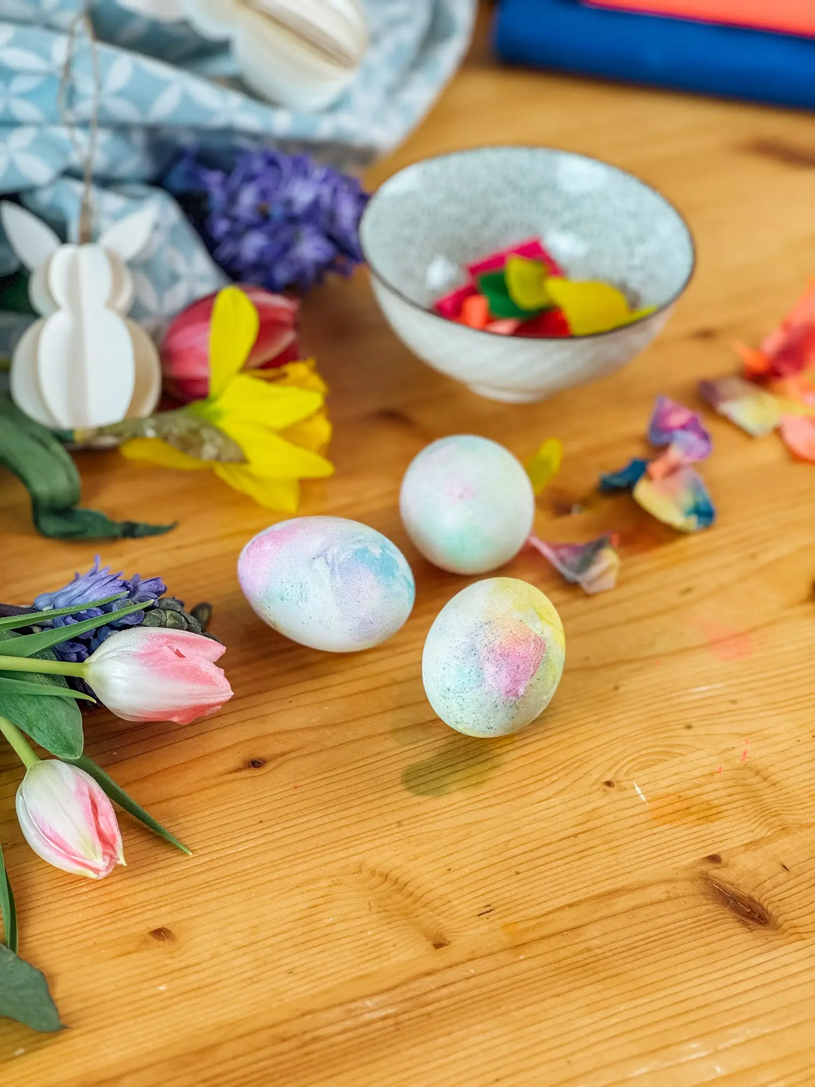 Eier, eingefärbt mit Krepppapier, trocknen auf einem Rost, umrahmt von Bastelmaterialien.