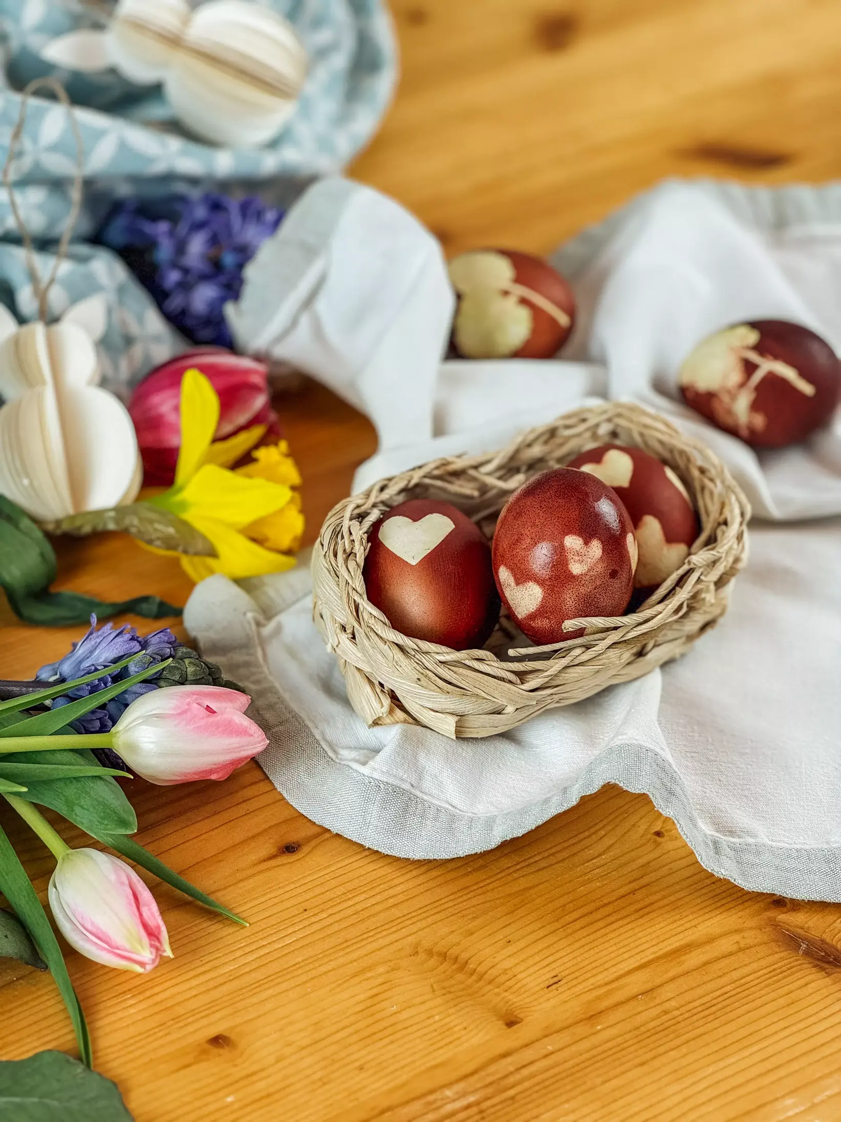 Ostereier, verziert mit Blättern und Blüten, nehmen beim Kochen in Zwiebelschalenwasser sanft ihre Farben an, umgeben von ihren natürlichen Zutaten.